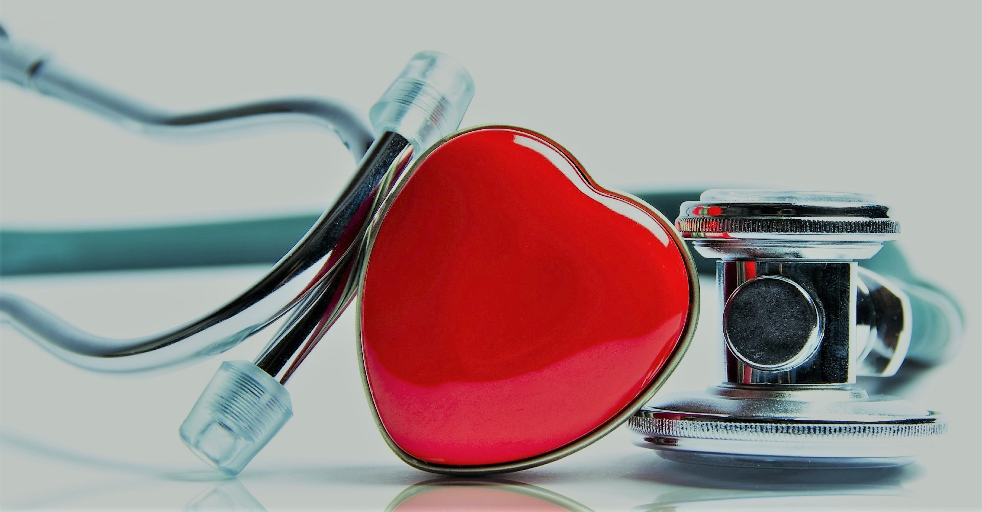 A red, plastic heart in the center of the photograph with a doctor's stethoscope leaning up against it and wrapping around.