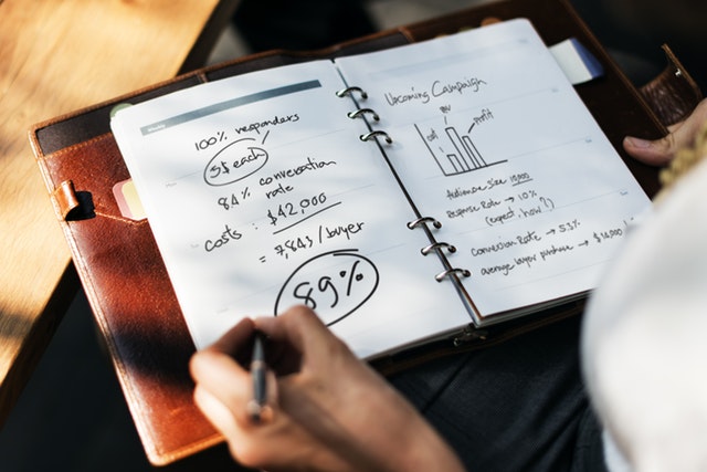 A person writing in a notebook which is filled with graphs, writing, and percentages.