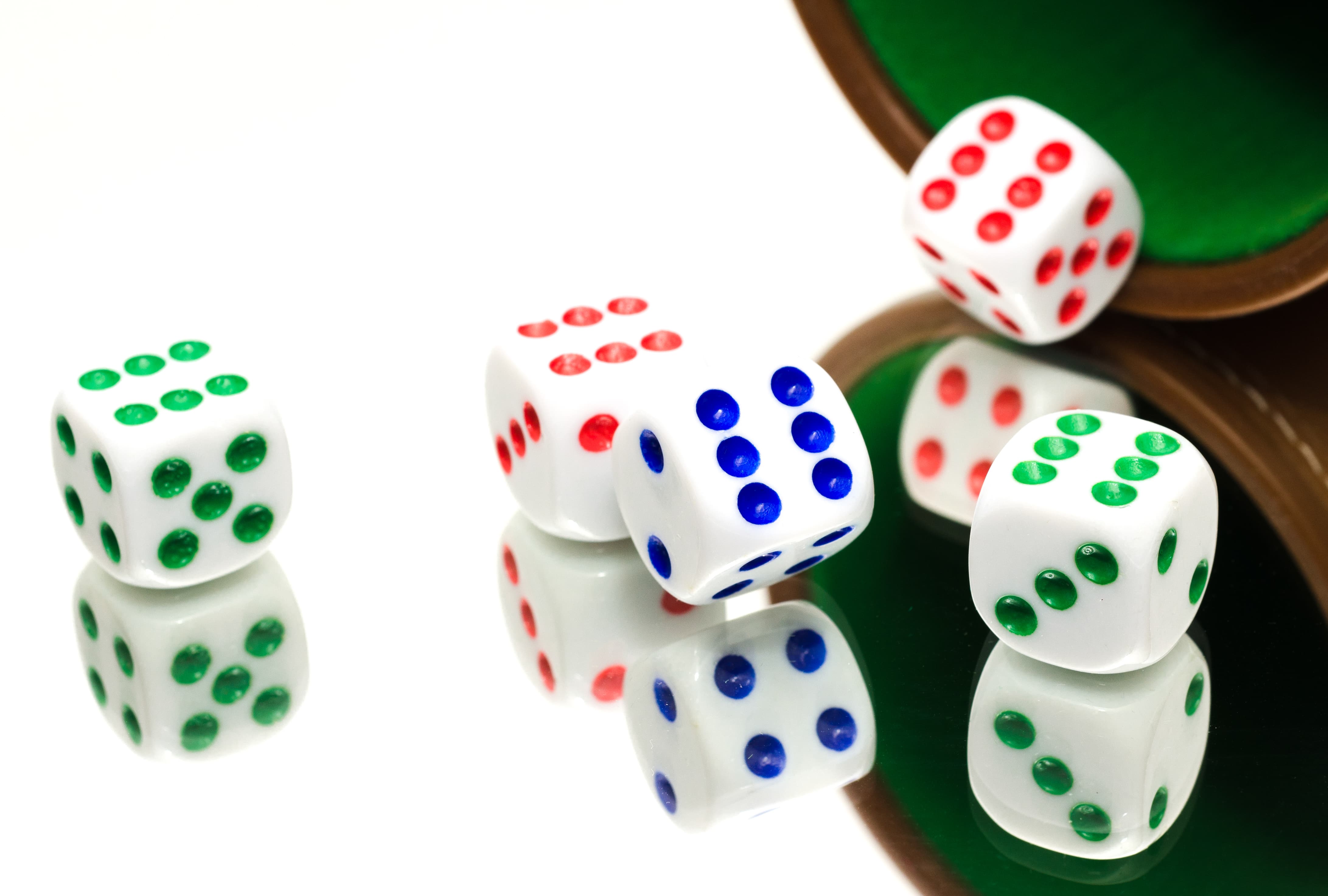 Several multicolored dice spilling out of a green-felted cup onto a reflective surface.